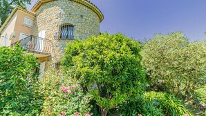 A stone tower with a balcony, surrounded by lush greenery and flowering plants.