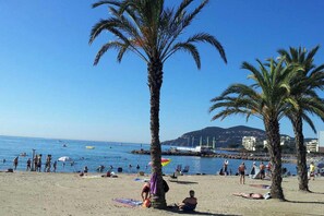 A beach with palm trees, people sunbathing, and boats in the water.