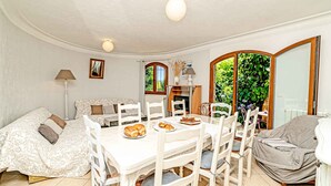 A dining area with a white table and chairs, a sofa, and a view of greenery outside.