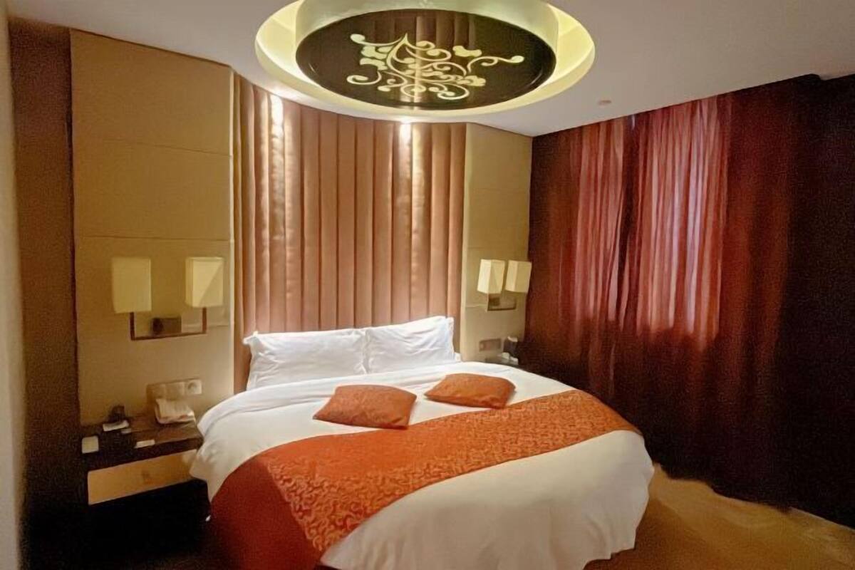 A hotel room with a bed, a nightstand, a mirror, and a wall-mounted light fixture.