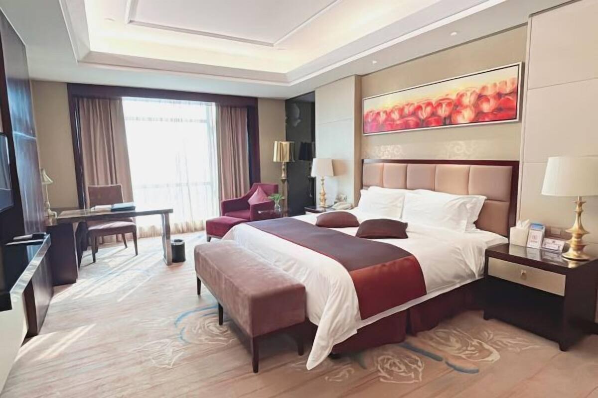 A hotel room with a large bed, a desk, a chair, and a TV.