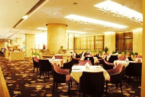 A hotel dining area with round tables, chairs, and a bar area in the background. - Guanfa Enjoy Hotel (Quzhou)