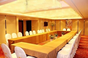 Un salón de conferencias con una mesa larga, sillas blancas y suelo alfombrado.