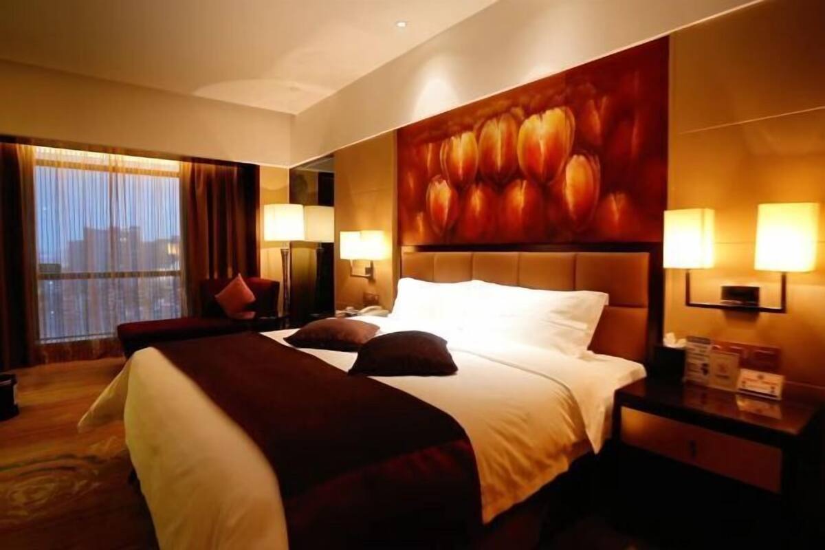 A hotel room with a large bed, two bedside lamps, a nightstand, and a large window with curtains.
