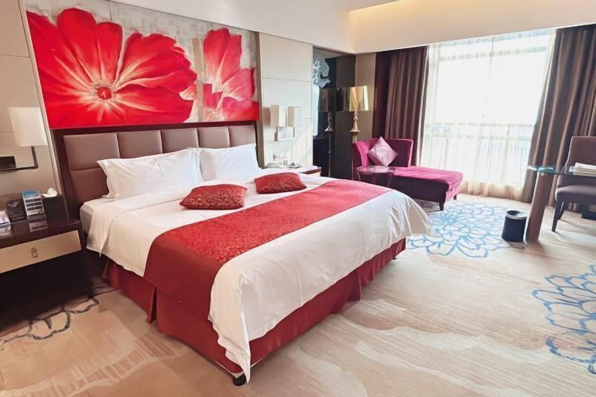 A hotel room with a large bed, a desk with a lamp, a TV, and a view of the outdoors.
