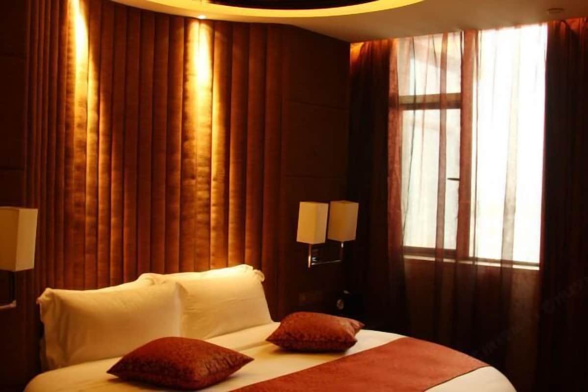 A hotel room with a large bed, two pillows, a bedside lamp, and a window with curtains.