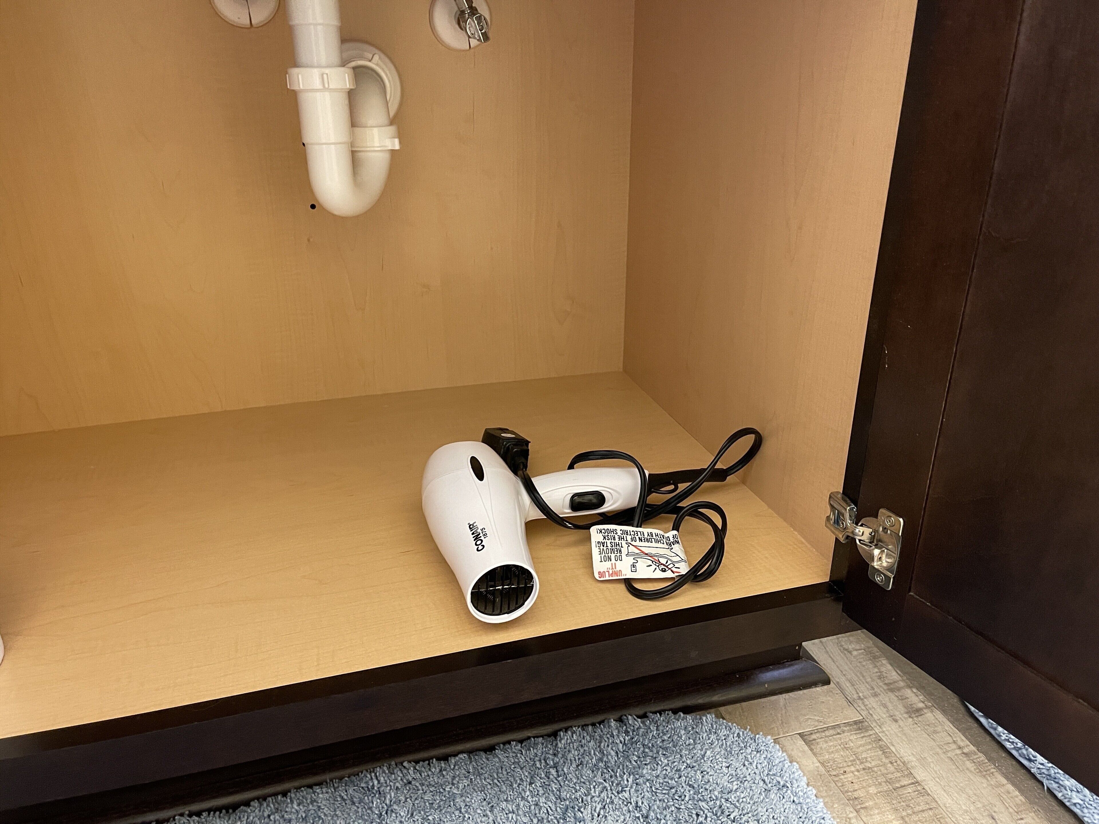A white portable heater with a power cord and a label on a wooden shelf.