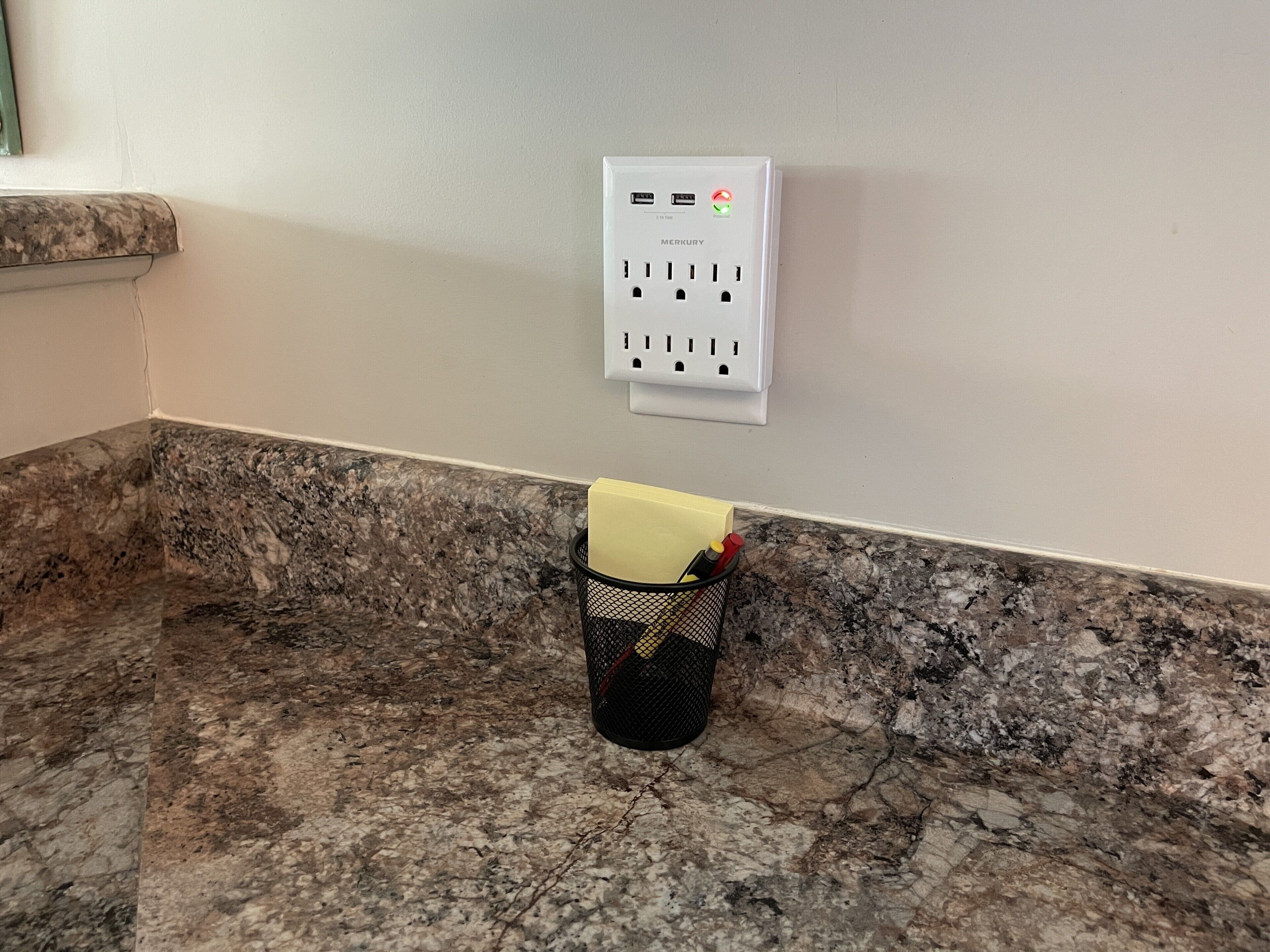 A white electrical outlet on a wall with a black mesh basket containing a yellow object and a red object.