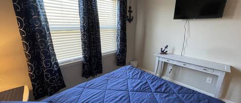 Une chambre à coucher avec un lit, un téléviseur fixé au mur, un bureau avec une chaise et des rideaux.