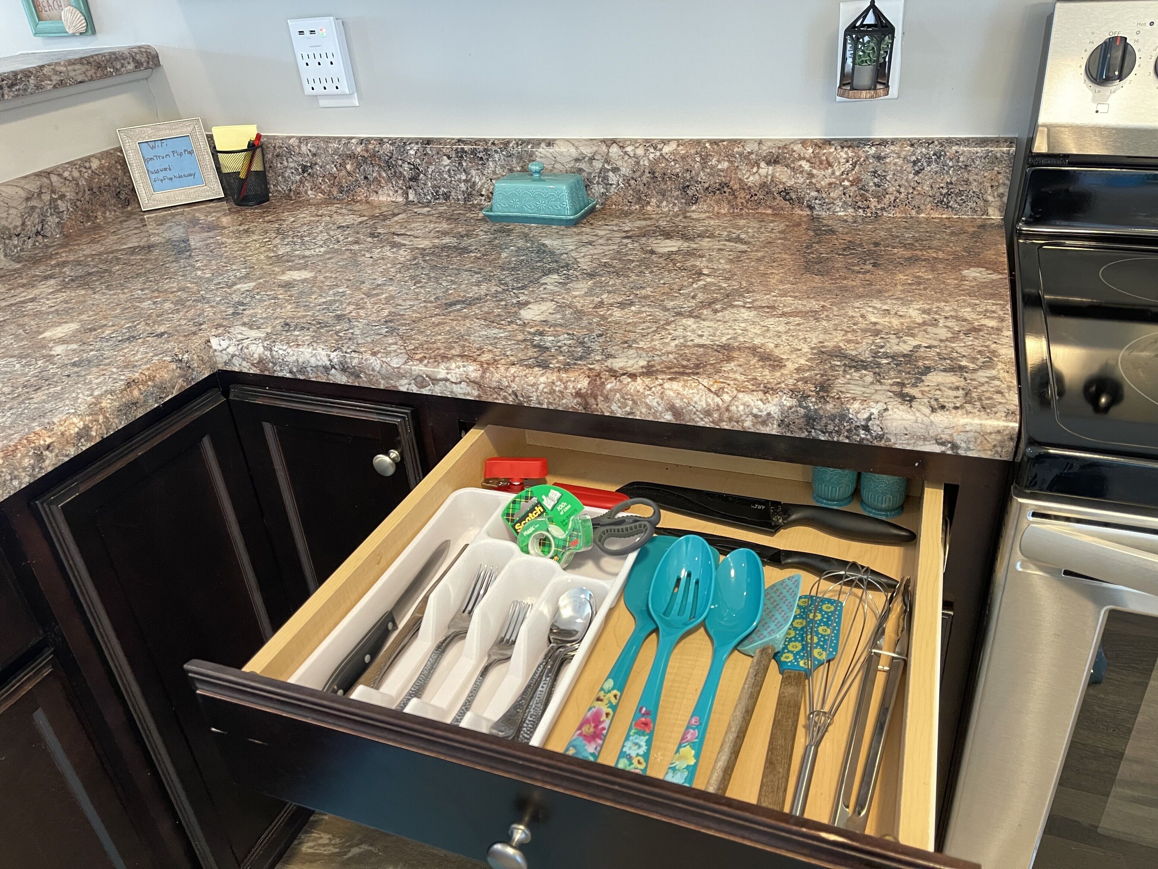 A kitchen with a granite countertop, a built-in oven, and a drawer with utensils.
