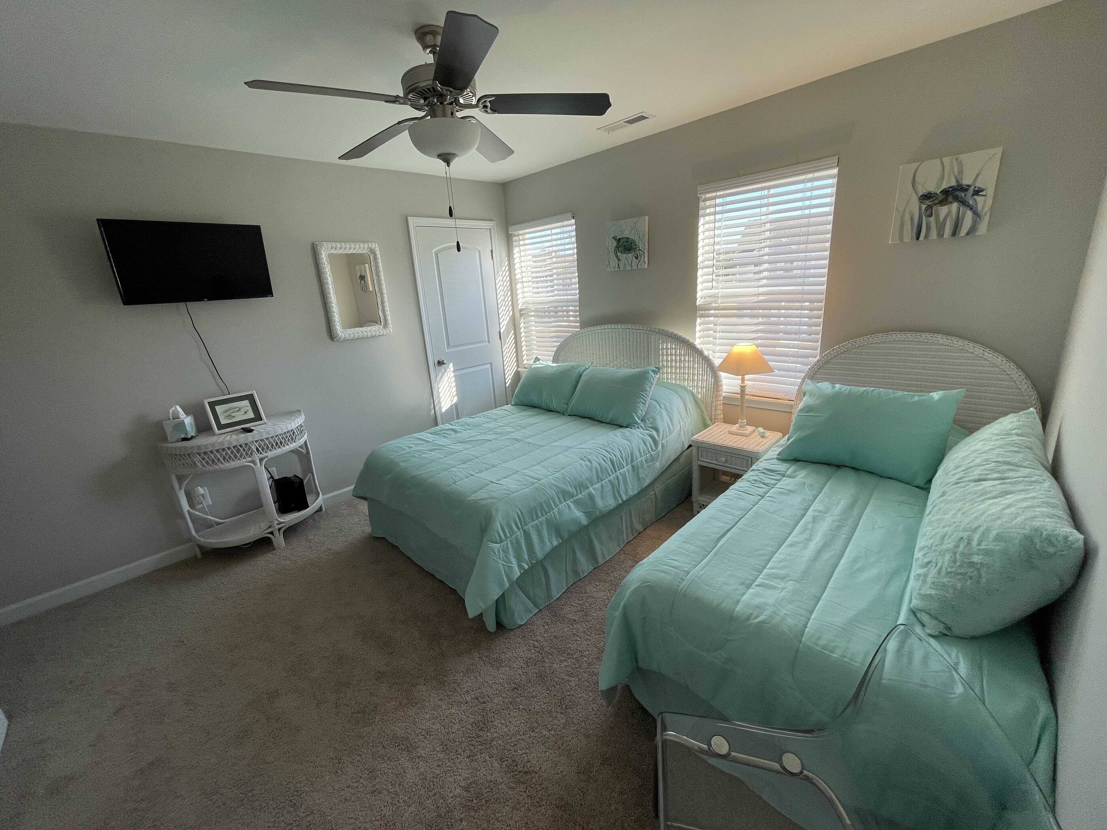 A bedroom with two beds, a ceiling fan, a TV, and artwork on the walls.