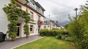 Un edificio residencial con terraza de madera, jardín con césped y una variedad de plantas.