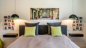 A bedroom with a large bed, two bedside tables, a wall-mounted picture, and a green pendant light.