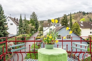 A balcony with a green table, a potted plant with yellow flowers, and a red railing. - Pet-Friendly Holiday Apartment 'Lichtentaler Allee' with Balcony and Wi-Fi (Baden-Baden)