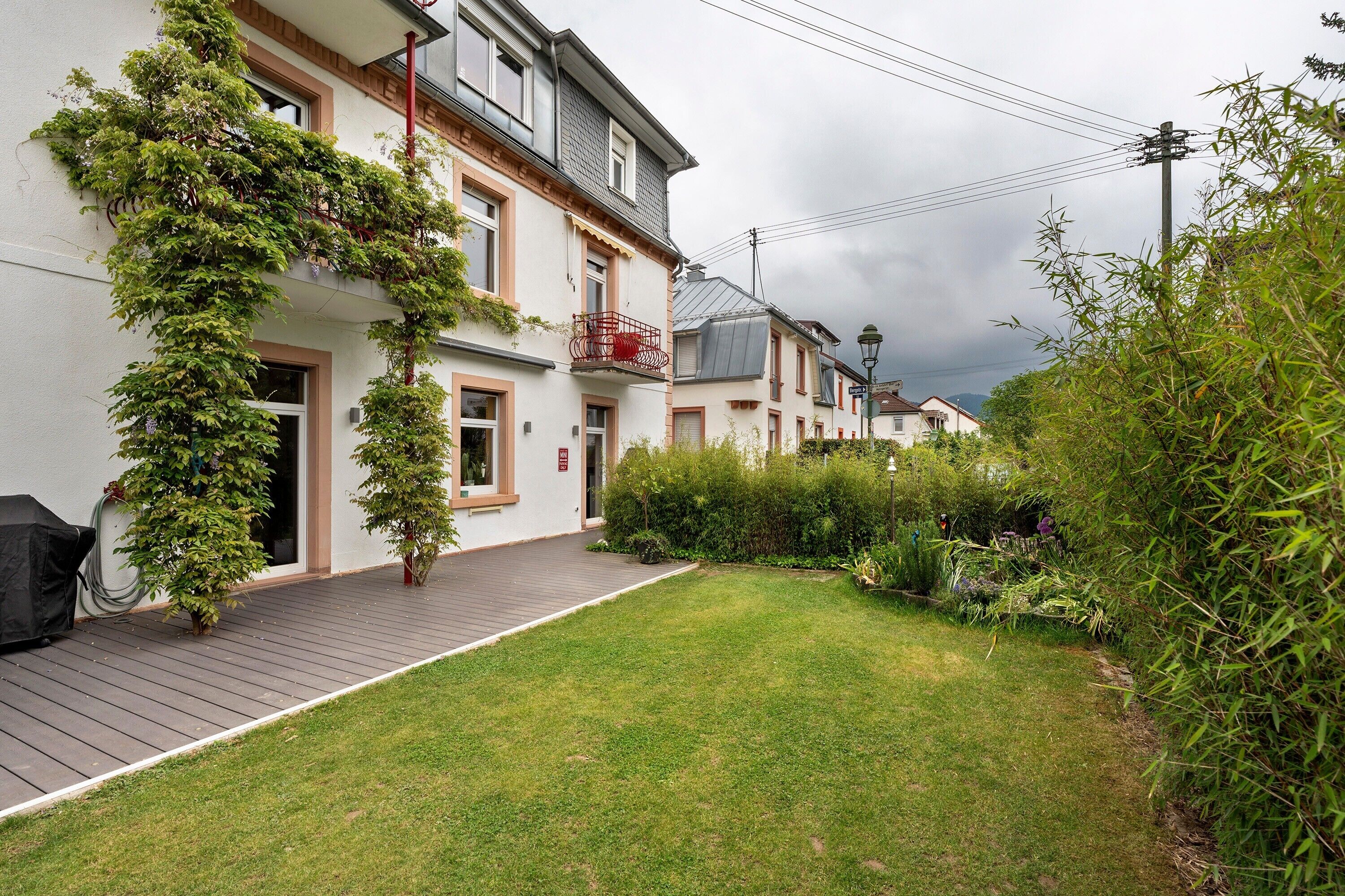 Edificio residenziale con veranda in legno, cortile con prato e giardino con diverse piante.