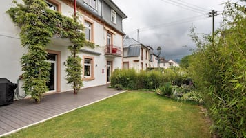 Edificio residenziale con veranda in legno, cortile con prato e giardino con diverse piante.