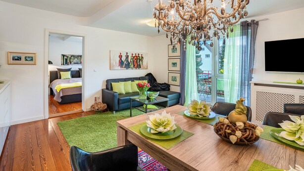 A modern living room with a dining area, a chandelier, a sofa, and a television.