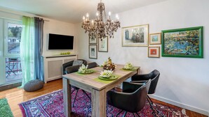 A dining area with a chandelier, a TV, framed artwork, and a table set with a centerpiece.