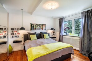 A bedroom with a bed, bedside lamps, a large window with curtains, a wall-mounted picture, and a radiator. - Pet-Friendly Holiday Apartment 'Lichtentaler Allee' with Balcony and Wi-Fi (Baden-Baden)