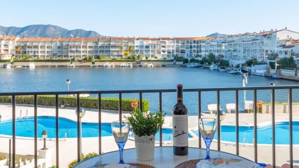A poolside view with a table, a bottle of wine, and a glass. - Sant Maurici by Interhome (Empuriabrava)