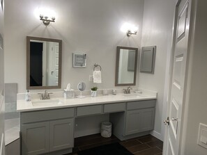 Une salle de bain moderne avec un meuble-lavabo à deux vasques, deux miroirs fixés au mur, un porte-serviettes et une petite plante en pot.