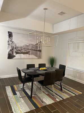Un coin repas avec une table ronde, des chaises noires, un lustre moderne et un tableau représentant un paysage urbain accroché au mur.