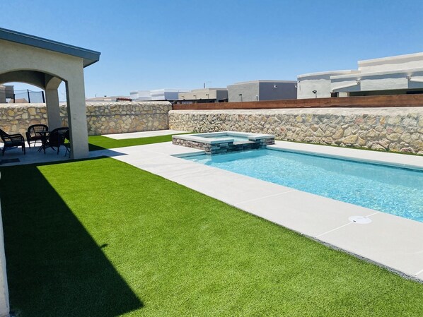 Une piscine avec un mur en pierre et une pelouse artificielle.