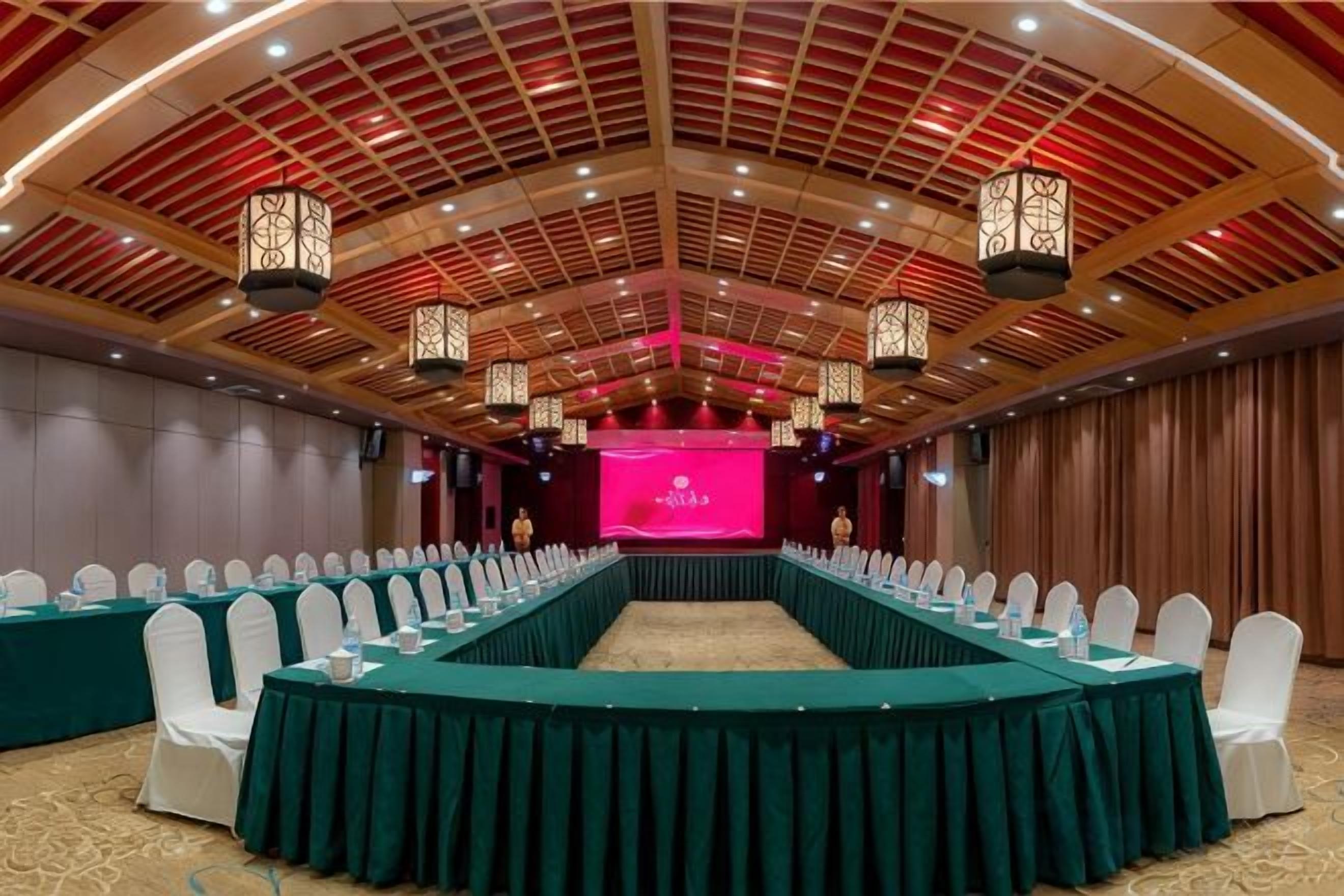 A conference room with a long table, white chairs, and a stage with a pink backdrop.