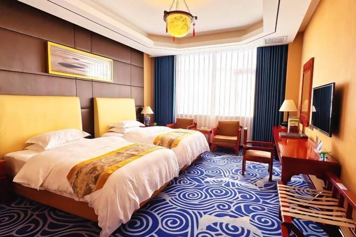 A hotel room with two beds, a desk, a chair, a television, and a large window with curtains.