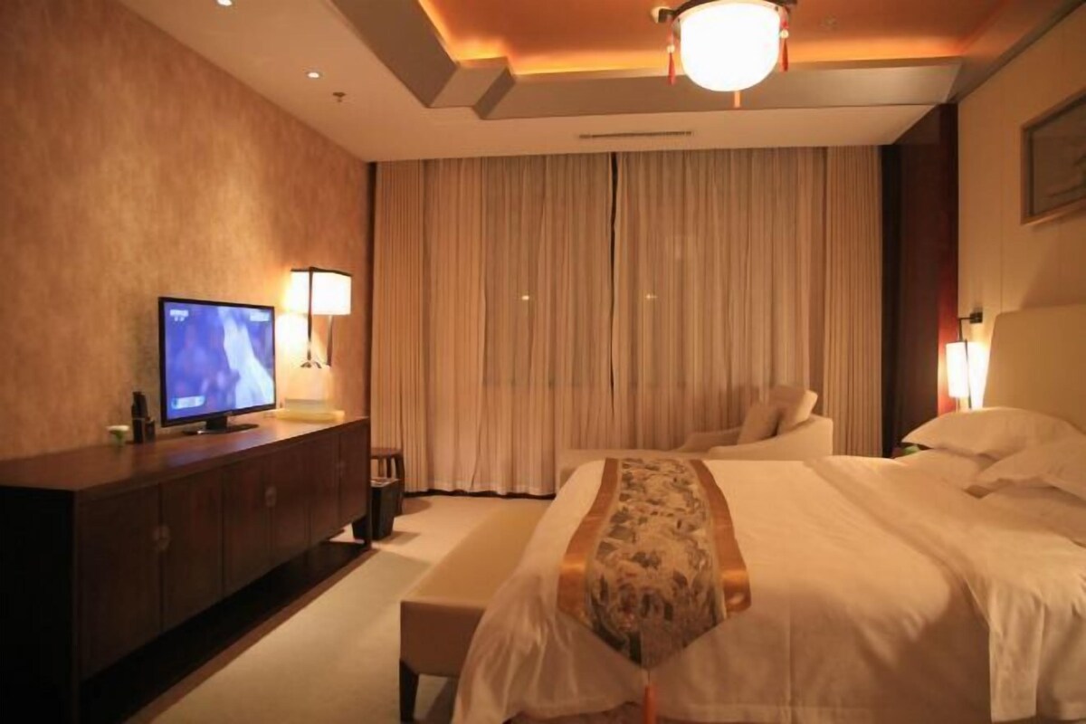 A hotel room with a large bed, a TV on a wooden cabinet, and a curtain-covered window.