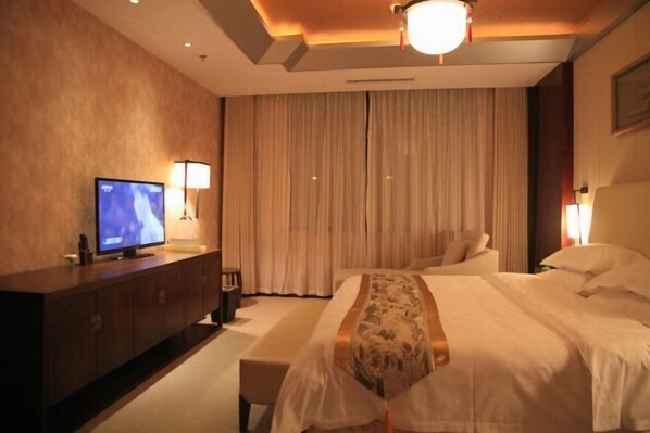 A hotel room with a large bed, a TV on a wooden cabinet, and a curtain-covered window. - Shuihu Hotel (Liangshan)