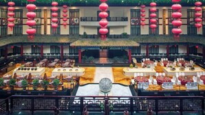 Une cour traditionnelle chinoise, ornée de lanternes rouges, avec une fontaine centrale et plusieurs espaces aménagés pour les repas.