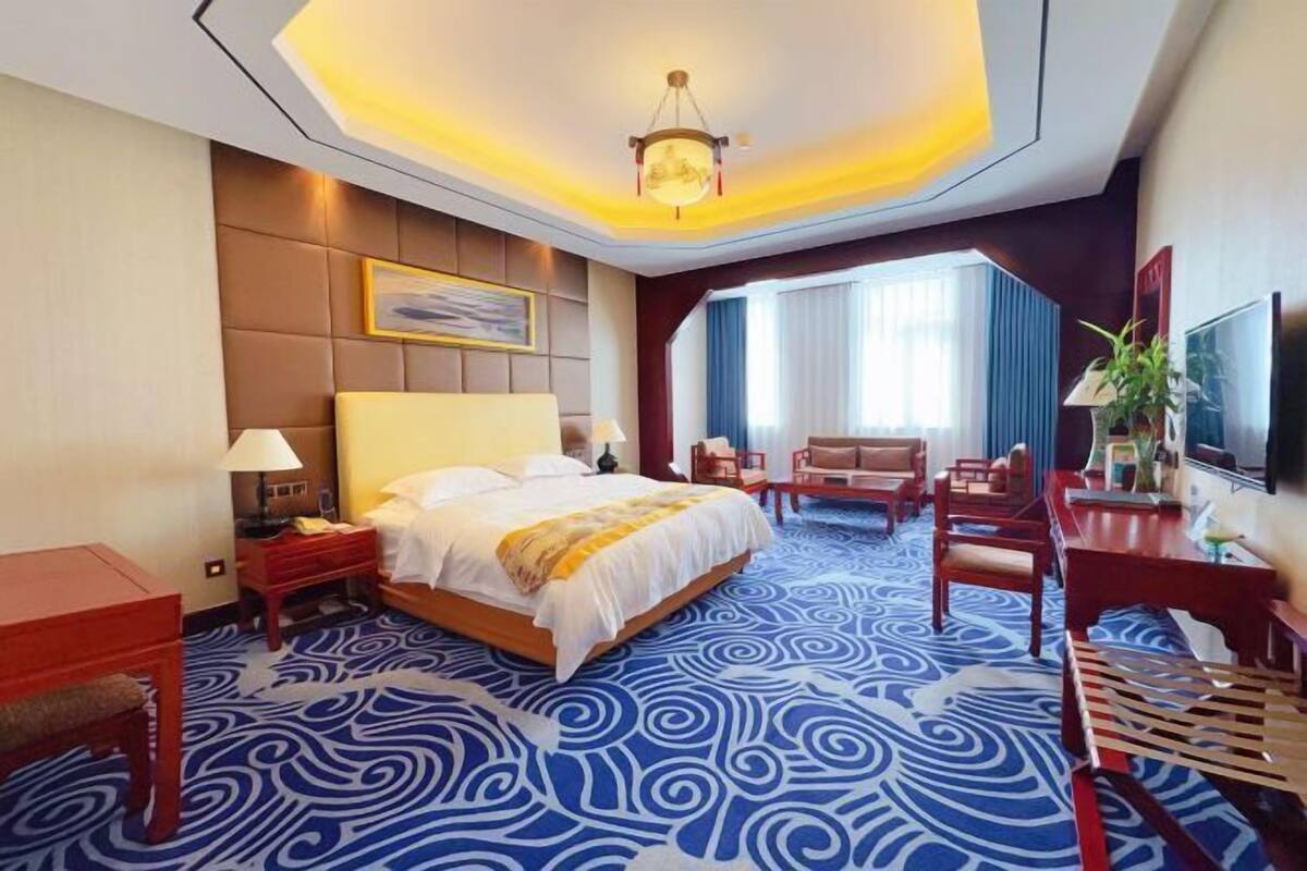 A hotel room with a large bed, a desk, a chair, a TV, and a window with curtains.