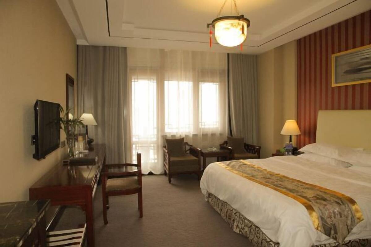 A hotel room with a large bed, a desk with a chair, a television, and a lamp.