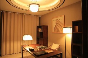 A room with a wooden desk, a lamp, a bookshelf, and a painting on the wall. - Shuihu Hotel (Liangshan)