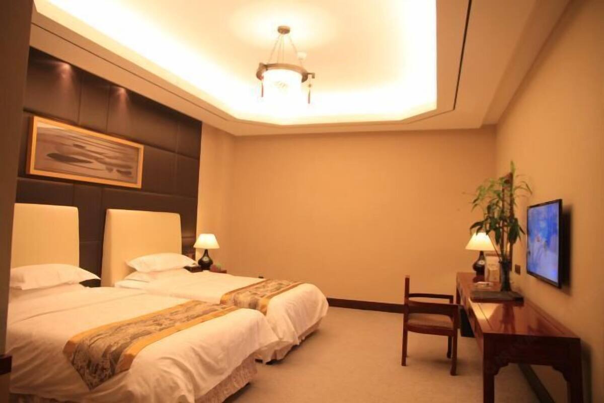 A hotel room with two beds, a desk, a chair, a television, and a ceiling light.
