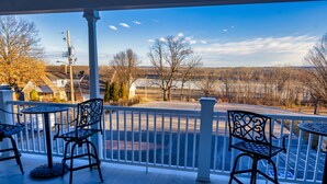 A covered outdoor area with two tables and two chairs, a white railing, and a view of a road and trees. - The Inn at Elijah McLeans (Washington)