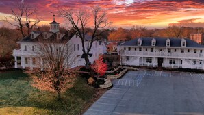 A large white building with a central tower, a parking lot, and a tree with red leaves. - The Inn at Elijah McLeans (Washington)