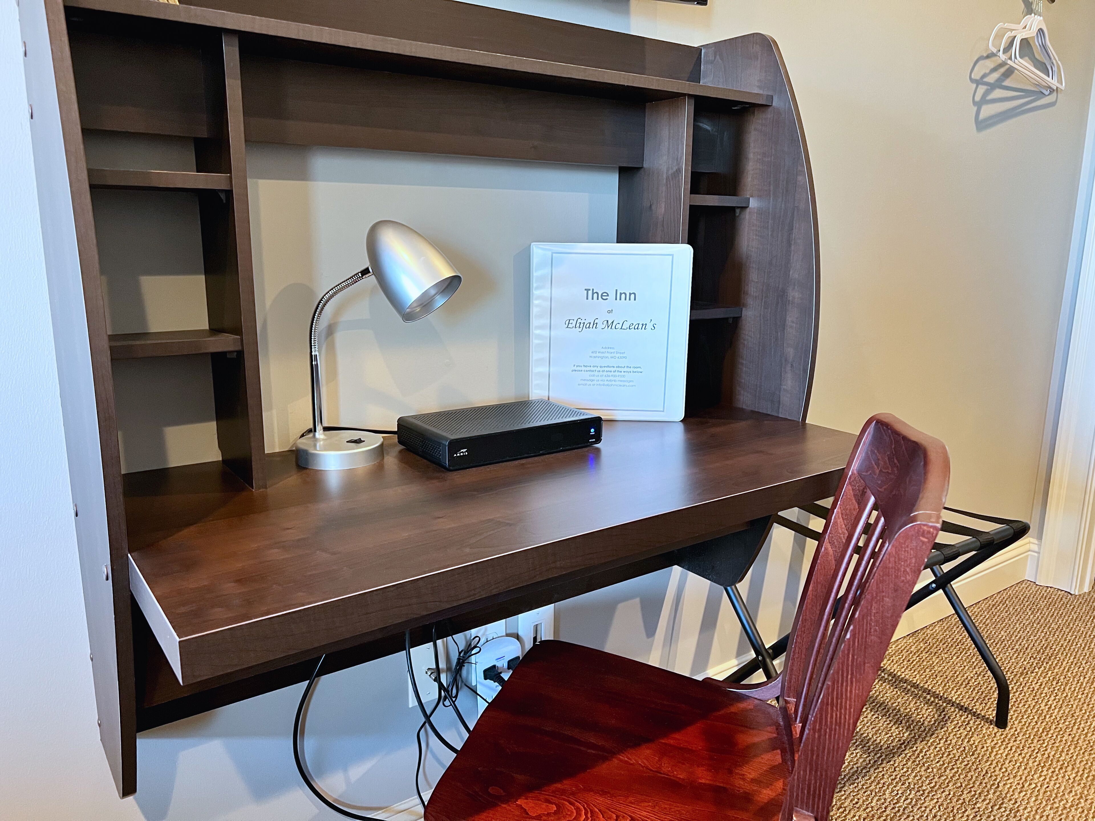 Un escritorio de madera con una lámpara, un letrero que dice 'The Inn at Elijah McLean's' y una silla roja.