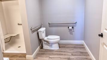 Un baño con inodoro, ducha y barra de apoyo.