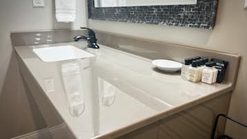 Un baño con un lavamanos blanco, un grifo negro y un espejo con un salpicadero blanco y negro. Hay artículos de aseo en la encimera.