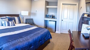 A hotel room with a bed, bedside table, lamp, chair, desk, microwave, refrigerator, and a door. - The Inn at Elijah McLeans (Washington)