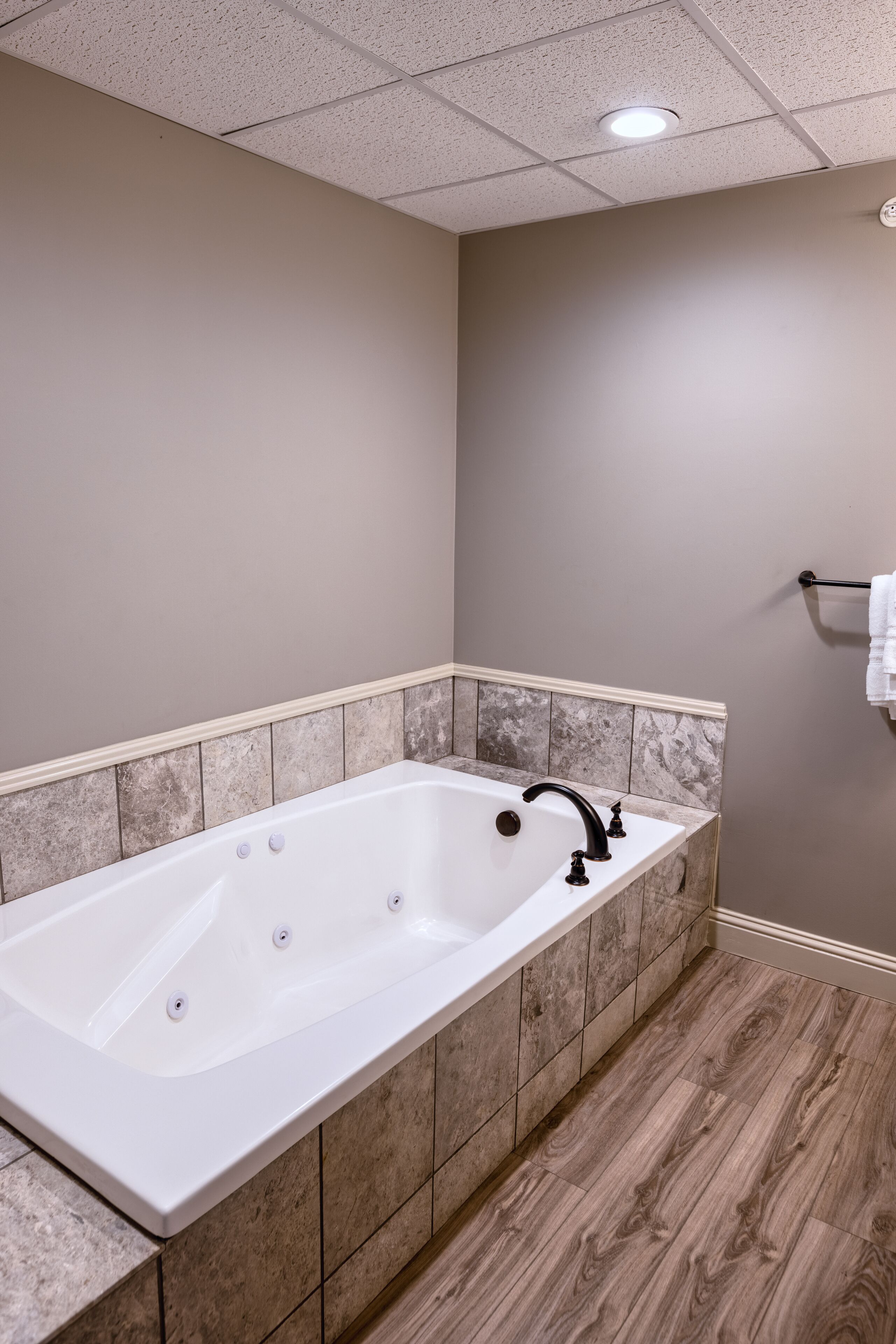 Un baño moderno con una bañera independiente, paredes de azulejos y piso de madera.