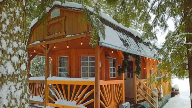 A wooden cabin with a porch and steps, surrounded by snow.