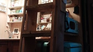 A wooden interior with a metal ladder, a blue refrigerator, and shelves with kitchen items.