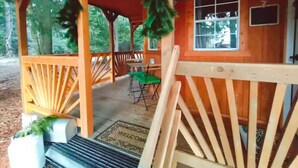 A wooden cabin with a porch, a dining table, and chairs.