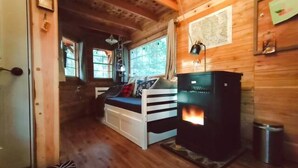 A cozy cabin interior with a wooden floor, a bed with pillows, a fireplace, and a map on the wall.