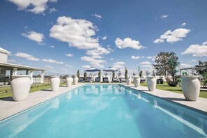 A swimming pool with lounge chairs and umbrellas, surrounded by large planters and a clear sky.