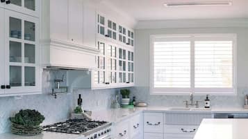 A kitchen with white cabinetry, a gas stove, a sink, and a window with blinds.