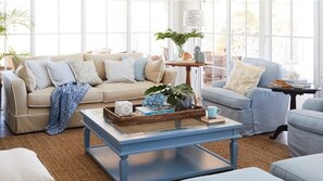 A well-lit living room with a beige sofa, a blue coffee table, and a light blue armchair.